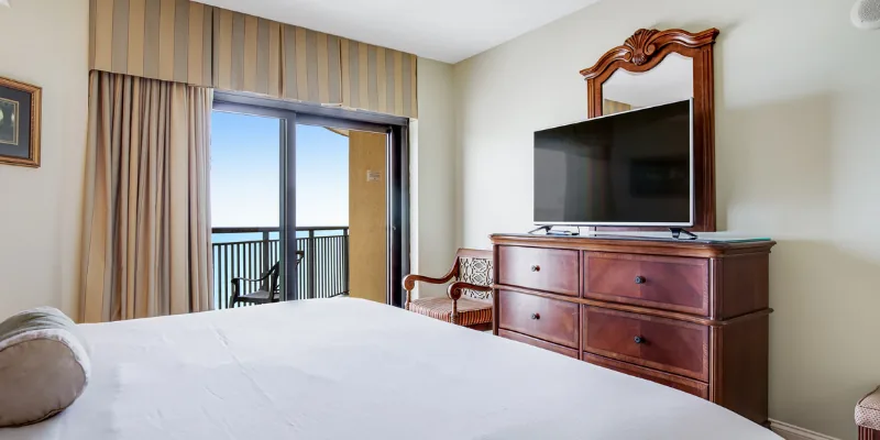 A hotel room with a large bed, dresser, TV, and balcony
