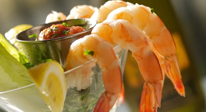 A glass of shrimp cocktail with cocktail sauce, lemons, and ice.