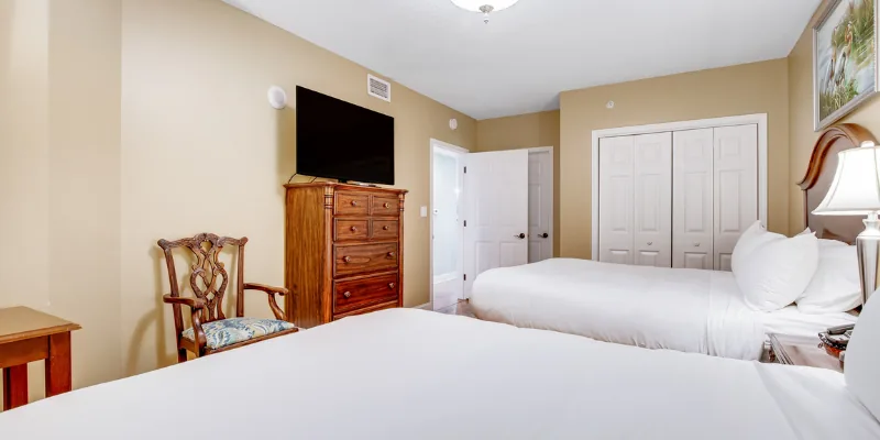 A wide view of a hotel room with two beds, a TV on a dresser, a closet, and a chair.