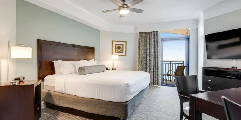 A hotel room with a king-size bed, balcony, flat-screen TV, and desk.