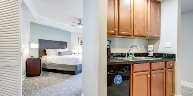 A room with a kitchenette and a bedroom in the background