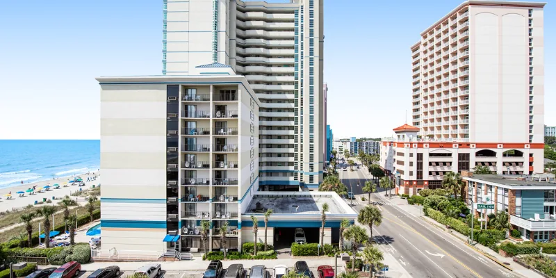 A wide exterior view of a high-rise building with a beach and ocean in the background.